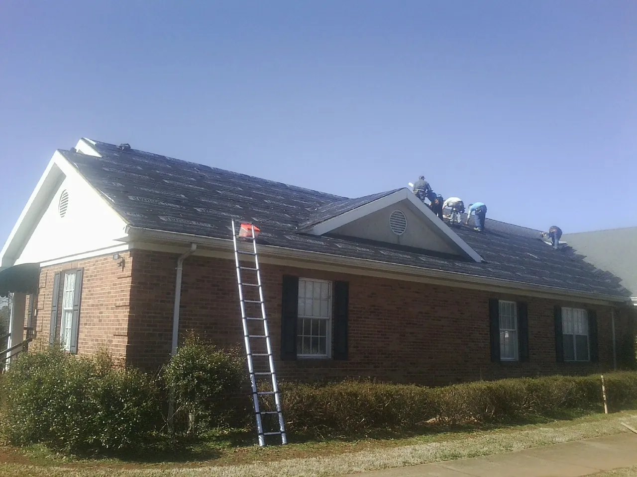 Crew tearing shingles off a brick ranch roof with a ladder set — Emergency Roof Repair work by our crew in Mcloud