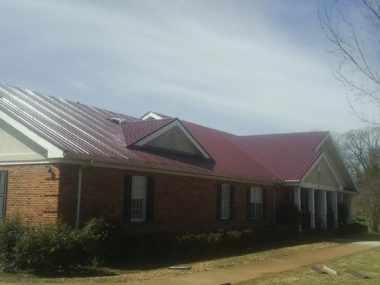 Red metal roof with gabled entries on a long brick building, from a Hail Damage Roof Repair job in Mcloud