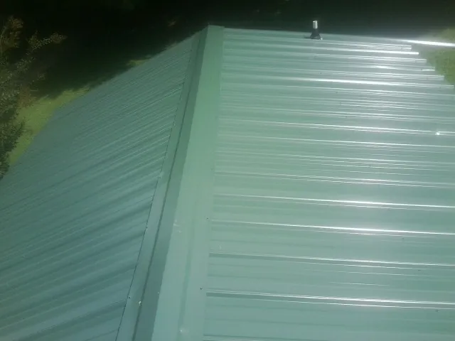 New green metal panels meeting at the ridge of a roof — Flat Roof Repair work by our crew in Mcloud