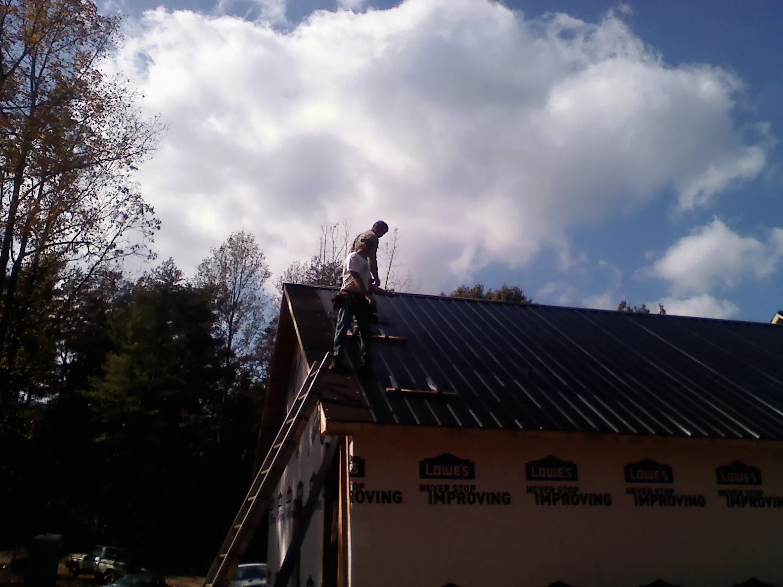 Roofer fastening dark metal panels high against a cloudy sky, from a Roof Inspection job in Mcloud