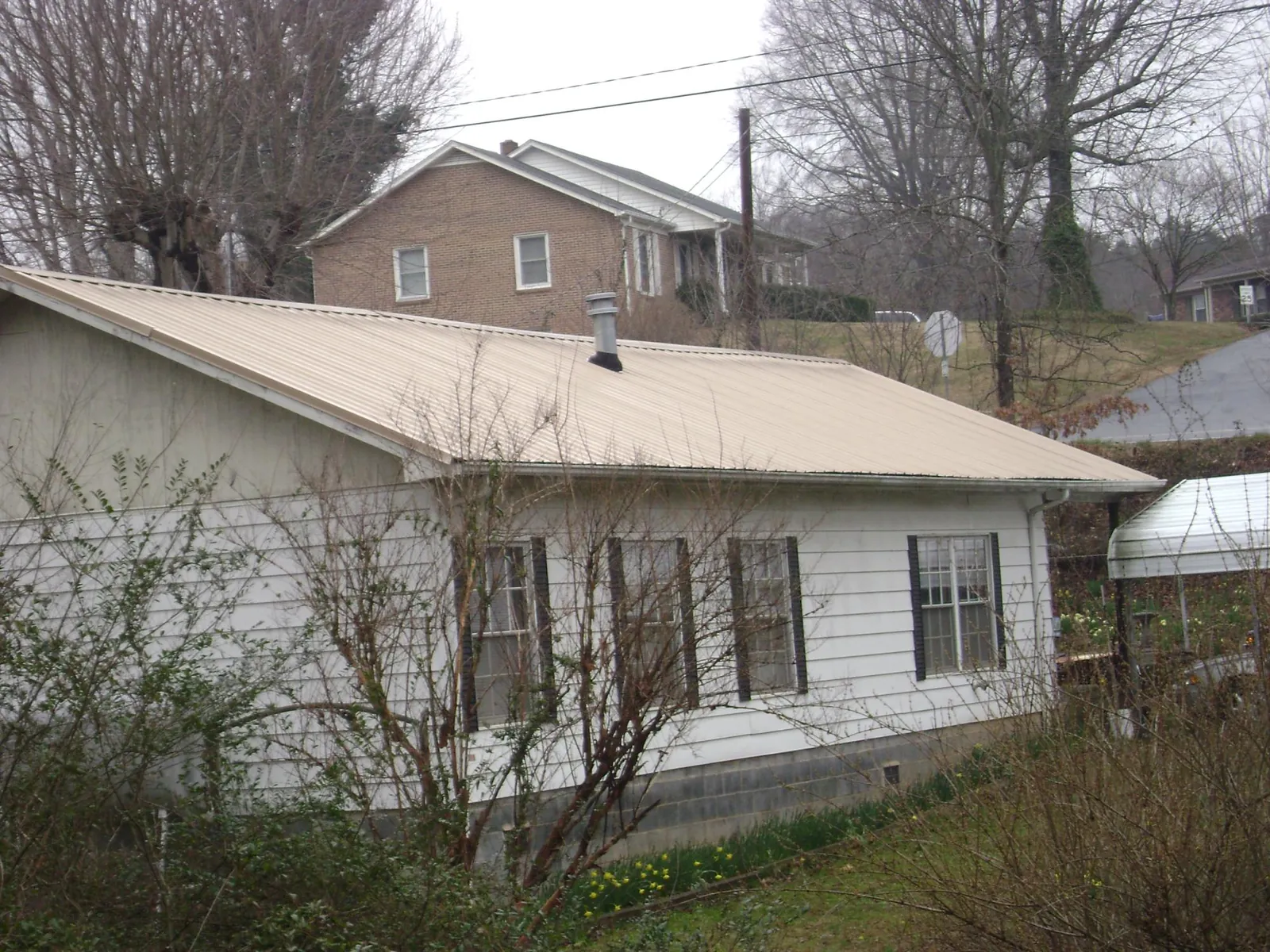 Tan metal roof on a white sided house set into a hillside — Commercial Roofing by Roofing Brothers in Mcloud
